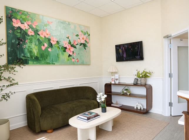Welcoming waiting room at Troy Meadows Dental with a green sofa and floral artwork